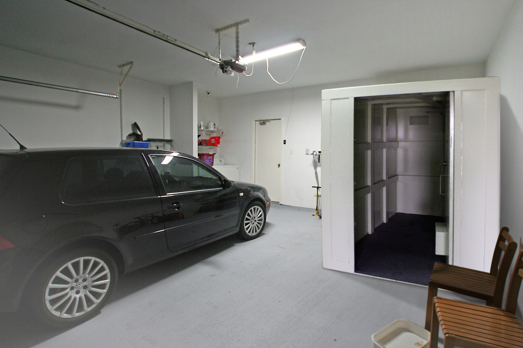 Car parked next to a safe room in a garage.