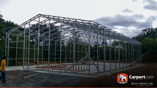 Commercial metal garage building framing on a concrete foundation with ladders laid inside.